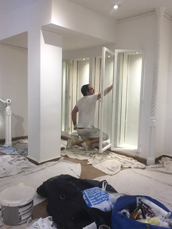 Painters in London. Painting an office in London. Painter painting glass  cupboards with a paint brush in hand with protective sheets on floor